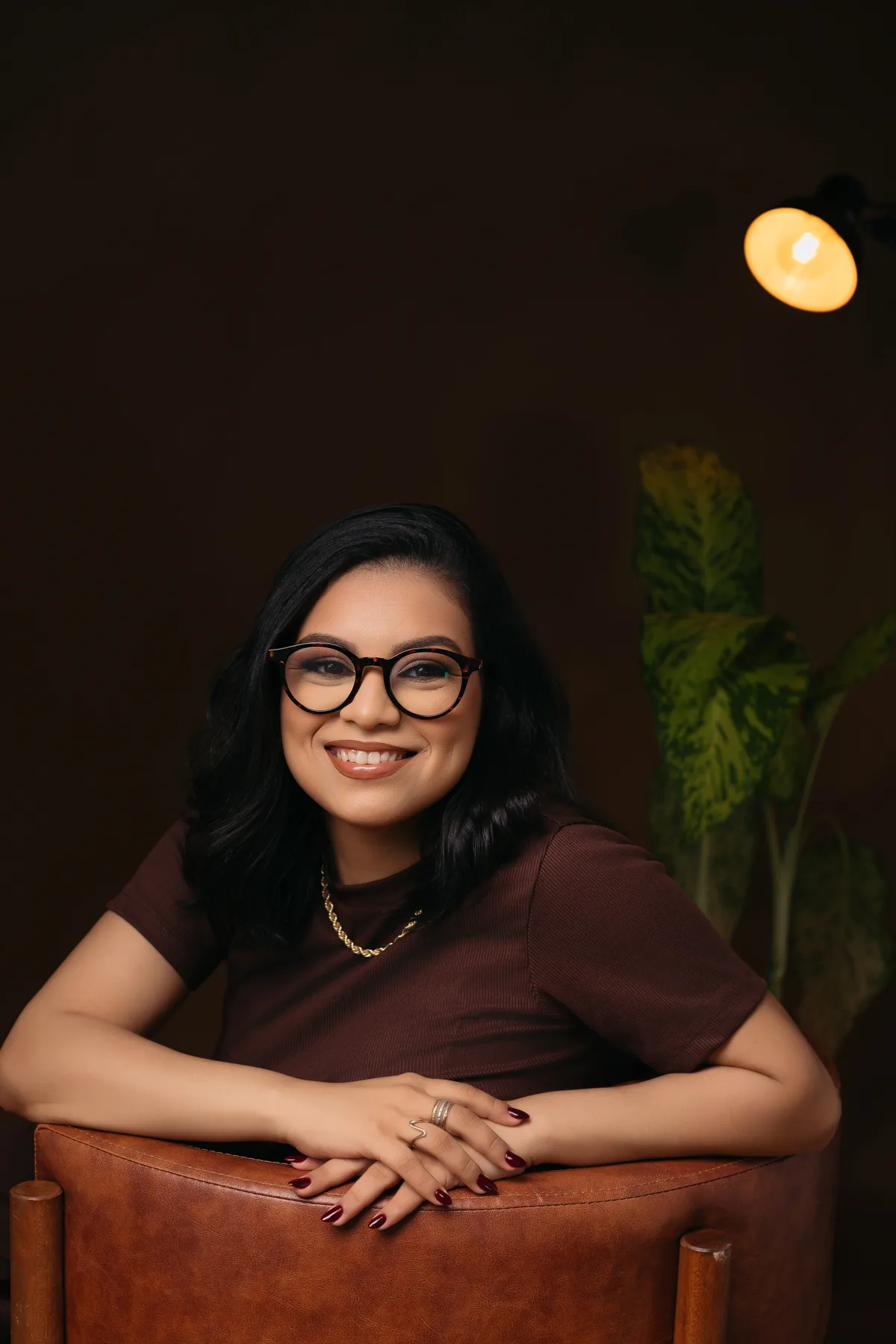Vitória Gonçalves sorrindo, apoiada no encosto de uma poltrona de couro